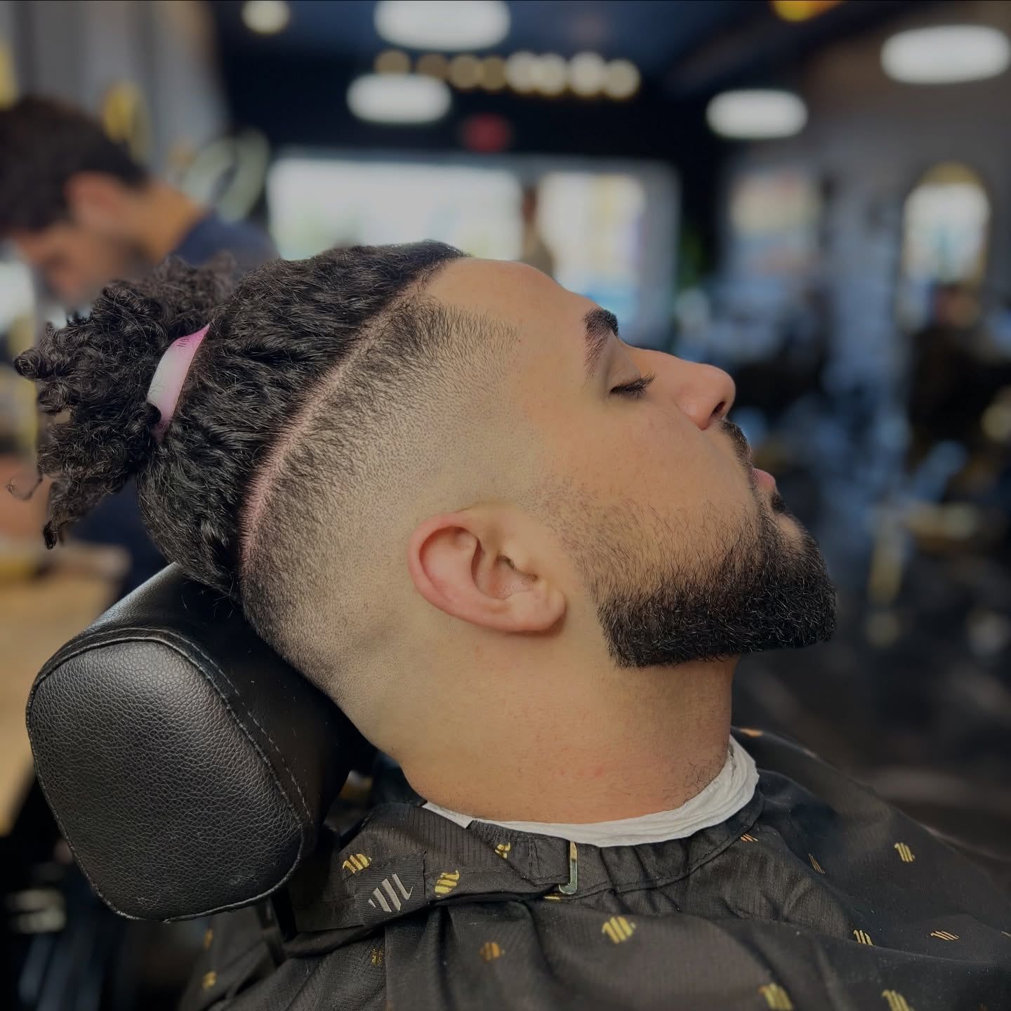 A client leaning back with a high fade, a shaved hard part and a sharp beard line