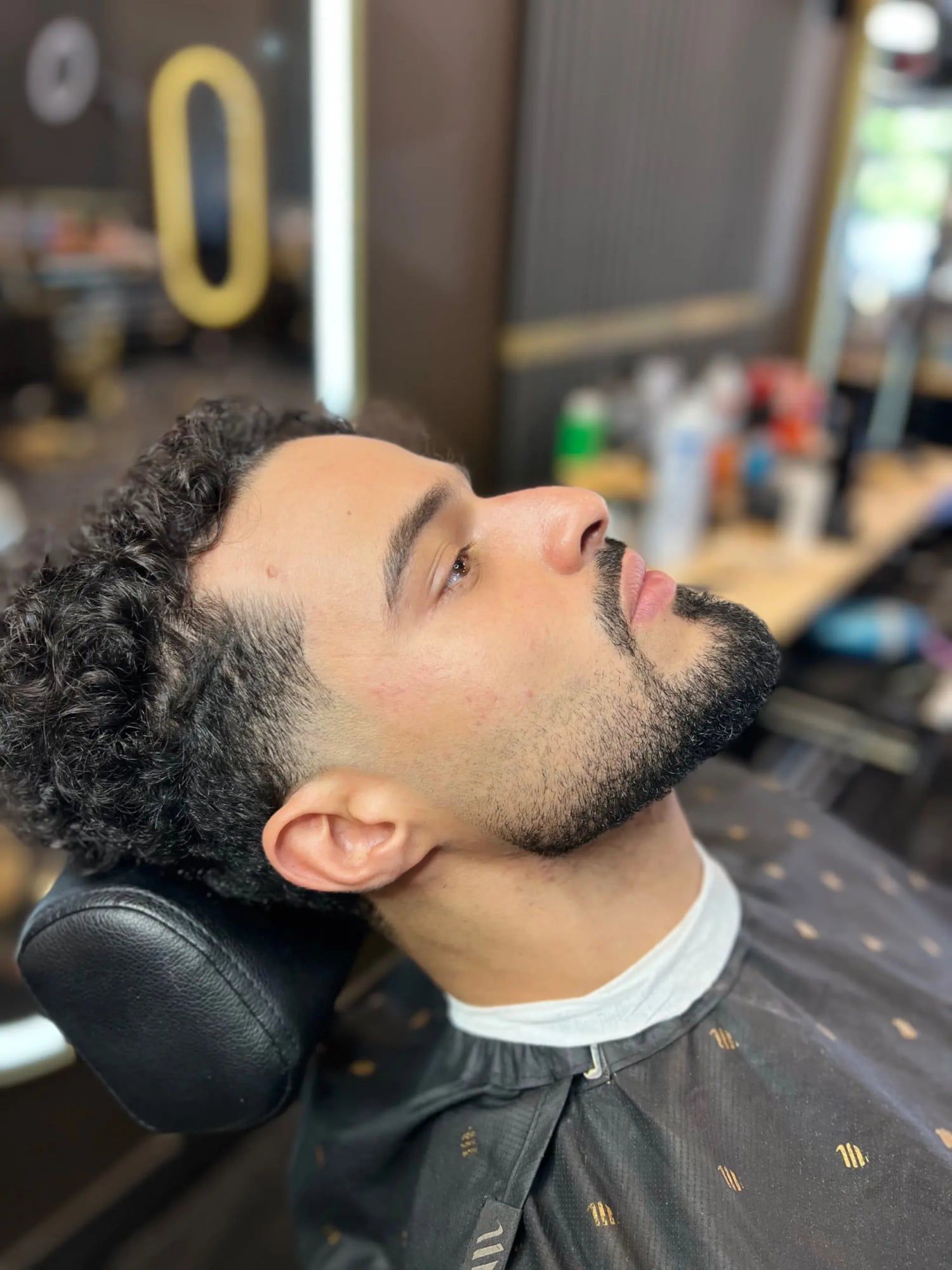 A client with curls on top, a low taper and a shaped beard